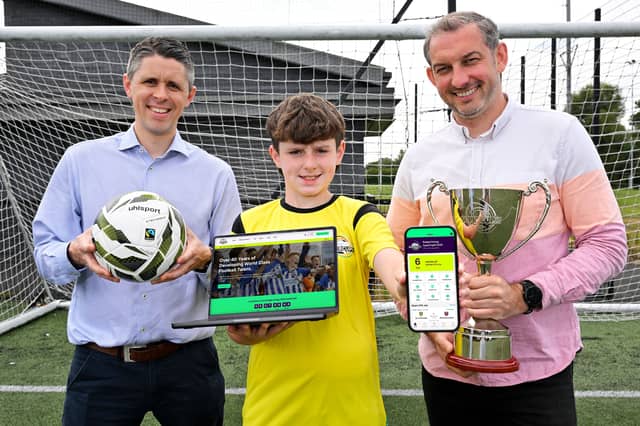 Sam Gamble, Tournament Co-ordinator of the Budget Energy SuperCupNI, Ryan Young, Creative Partner at Astutely, and budding young footballer Theo Lever are pictured launching the new official Budget Energy SuperCupNI website and mobile app ahead of the 2026 tournament.
