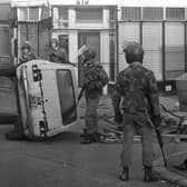 Troops on patrol in the Falls Road area of Belfast encounter a civilian by an overturned car that formed a barricade during rioting in 1981